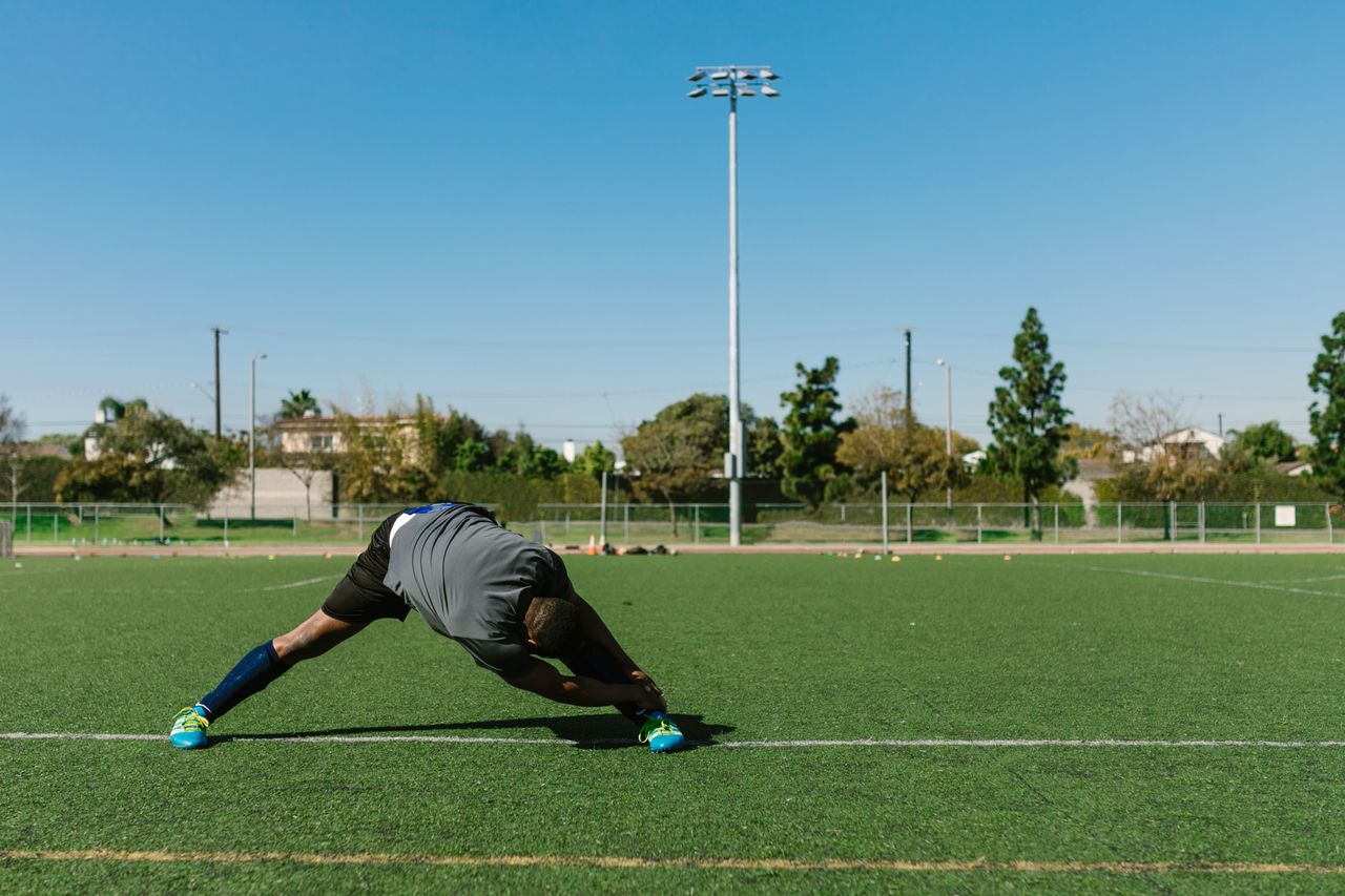 Athlete stretching on a soccer field during a sunny day, preparing for a workout.